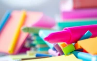 Highlighting text with a vibrant pink highlighter pen among colorful stationery.